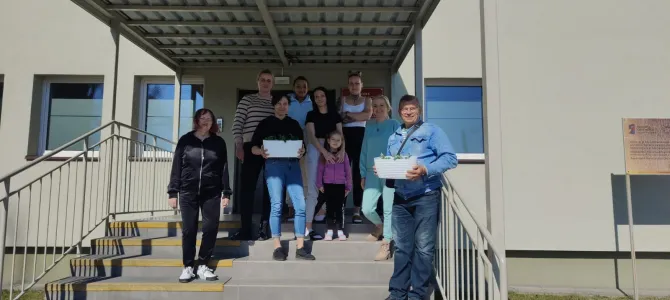 Na zdjęciu uczestnicy marcowego spotkania z mieszkańcami wraz z opiekunkami. Dwóch uczestników trzyma doniczki z posadzonymi kwiatami