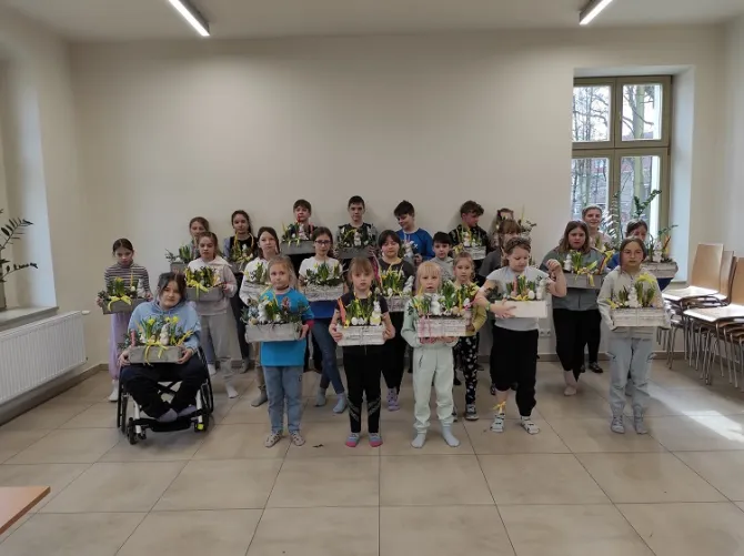 Grupowe zdjęcie uczestników warsztatów wielkanocnych, którzy w rękach trzymają wykonane przez siebie stroiki świąteczne.