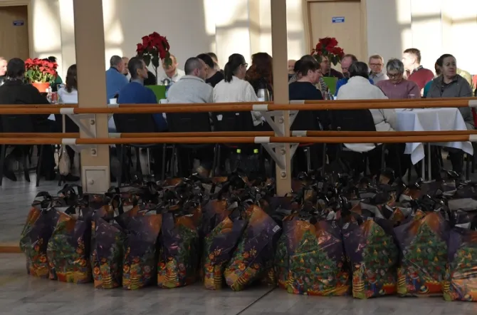 Na zdjęciu paczki świąteczne dla uczestników spotkania wigilijnego, w tle uczestnicy spotkania