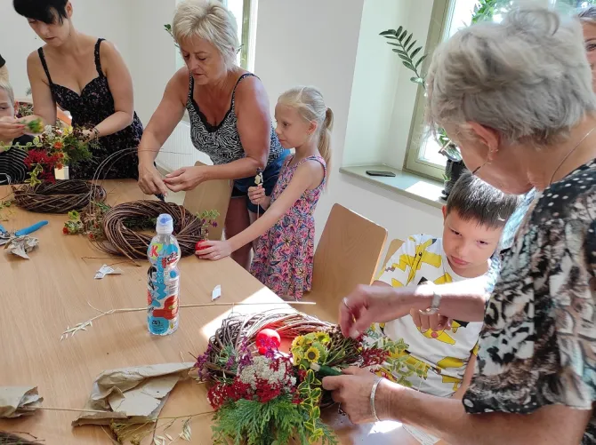 Na zdjęciu dzieci i osoby dorosłe wykonujące wianki podczas warsztatów florystycznych