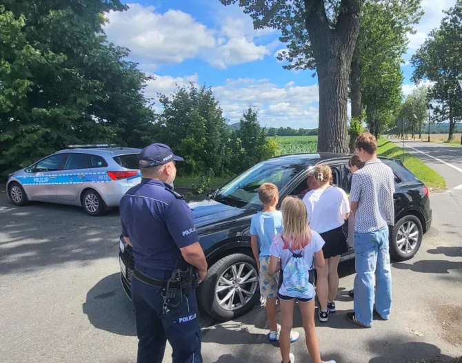 Wychowankowie Placówki Wsparcia Dziennego w dzielnicy Leszczyny wręczający ulotki kierowcy w obecności Policjanta