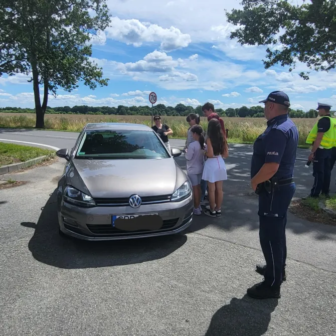 Wychowankowie Placówki Wsparcia Dziennego w dzielnicy Leszczyny wręczający ulotki kierowcy w obecności Policjantów